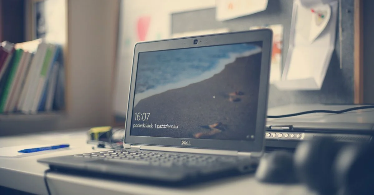 Un espace de travail contemporain avec un ordinateur portable Dell, des livres et des fournitures de bureau sur un bureau, reflétant les essentiels modernes du bureau.