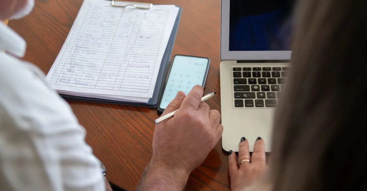 Deux adultes travaillant à un bureau avec un ordinateur portable, un smartphone et des documents. Scène de bureau collaboratif.