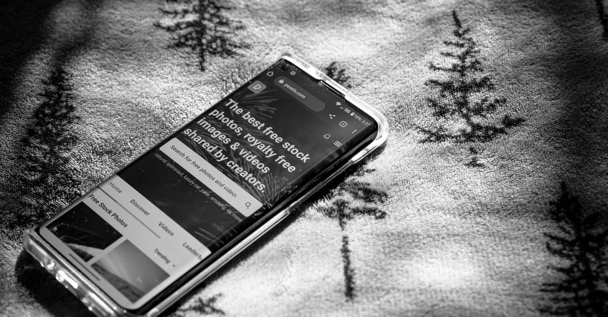 Photo en noir et blanc d'un smartphone sur une surface en tissu à motif d'arbre.