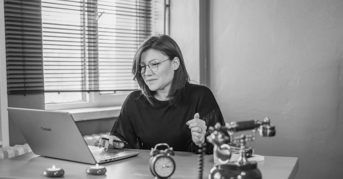Une femme d'affaires utilisant un ordinateur portable à son bureau avec un téléphone vintage et un réveil, créant un mélange d'ambiances modernes et rétro.