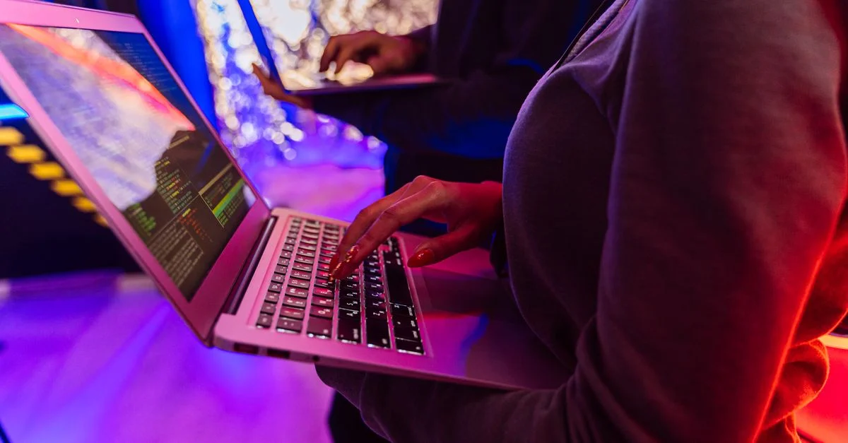 Deux professionnels analysant des données sur des ordinateurs portables avec un éclairage coloré, se concentrant sur les détails de la cybersécurité.