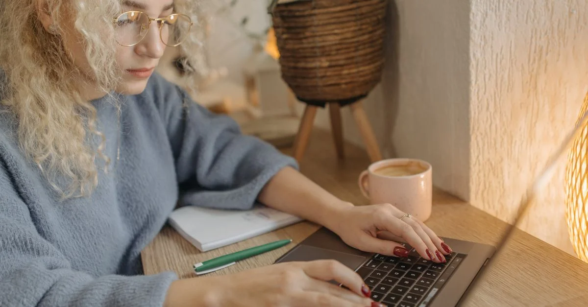 Femme concentrée aux cheveux bouclés travaillant sur un ordinateur portable dans un cadre intérieur confortable.