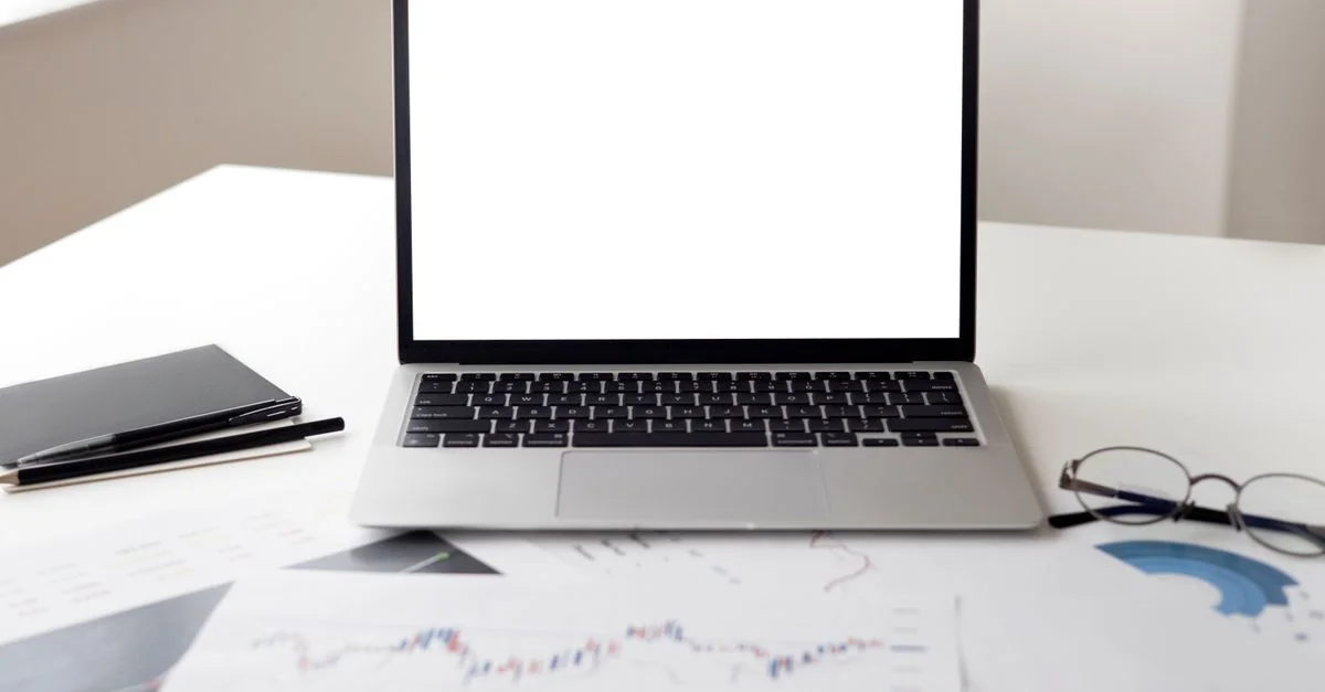 Ordinateur portable ouvert avec des documents financiers sur un bureau, idéal pour des thèmes d'entreprise et de technologie.